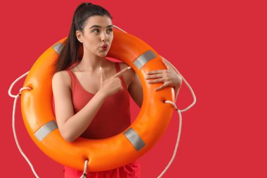 Kırmızı arka plandaki bir şeyi işaret eden yüzük şamandıralı bir kadın cankurtaran.