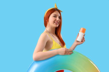 Güneş kremi sürmüş genç bir kadın ve mavi arka planda şişirilebilir bir yüzük.