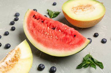 Gri arkaplanda taze karpuz, kavun ve yaban mersini.