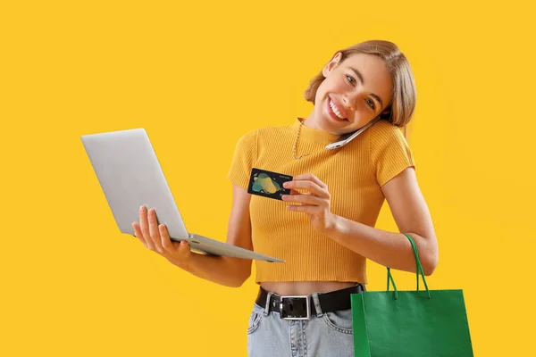 黄色の背景に携帯電話で話してクレジットカードとラップトップを持つ若い女性 オンラインショッピング — ストック写真