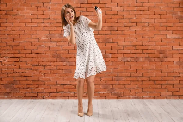 Scared young woman with pepper spray for self-defence near brick wall