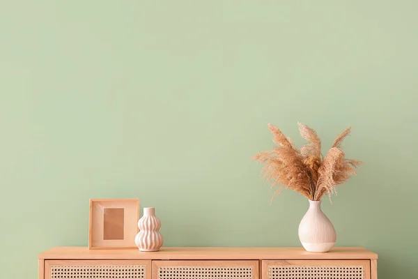 Modern chest of drawers with pampas grass and decor near green wall in room