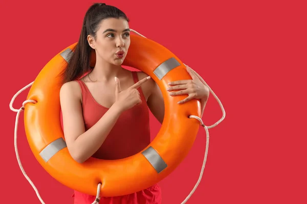 Female lifeguard with ring buoy pointing at something on red background