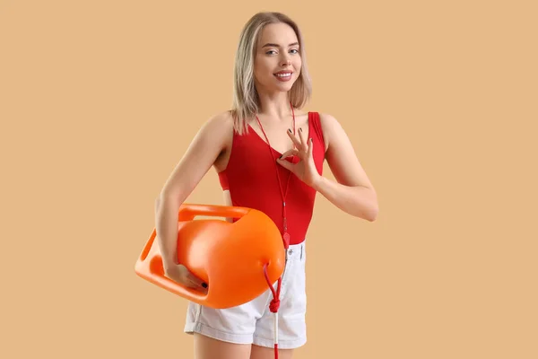 Female lifeguard with rescue buoy showing OK on beige background