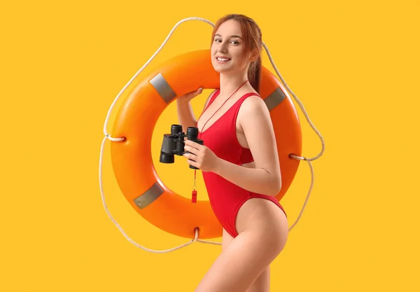 Female lifeguard with binoculars and ring buoy on yellow background