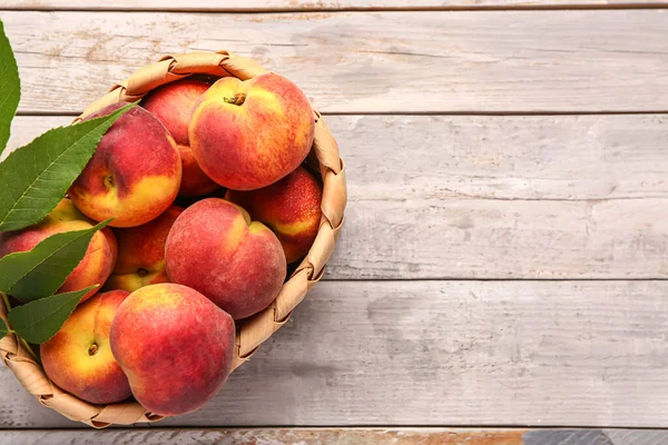 stock image Wicker bowl with sweet peaches and leaves on grey wooden background