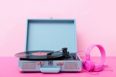 Pembe duvarın yanındaki masada vinil diski ve kulaklığı olan kayıt çalar