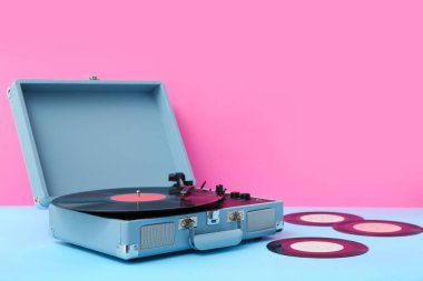 Pembe duvarın yanındaki masada vinil diskleri olan kayıt çalar