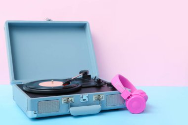 Pembe duvarın yanındaki masada vinil diski ve kulaklığı olan kayıt çalar