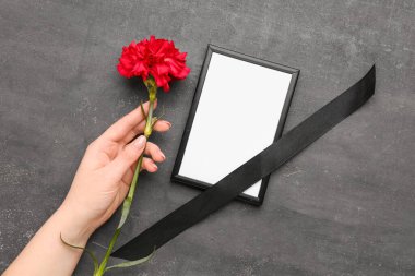 Koyu grunge arka planda siyah kurdeleli kırmızı karanfil ve fotoğraf çerçevesi tutan kadın.