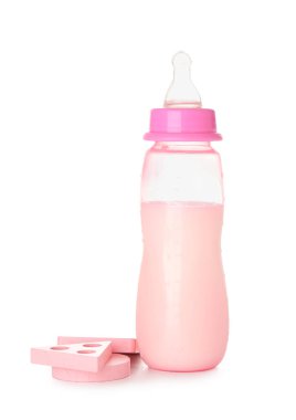 Beyaz arka planda oyuncakları olan bebek için bir şişe süt.