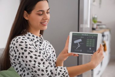 Akıllı ev güvenlik sistemi kontrol paneli olan genç bir kadın mutfakta, yakın plan.