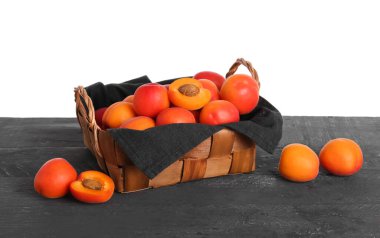 Masada beyaz arka planda olgun kayısılarla dolu bir hasır sepet.