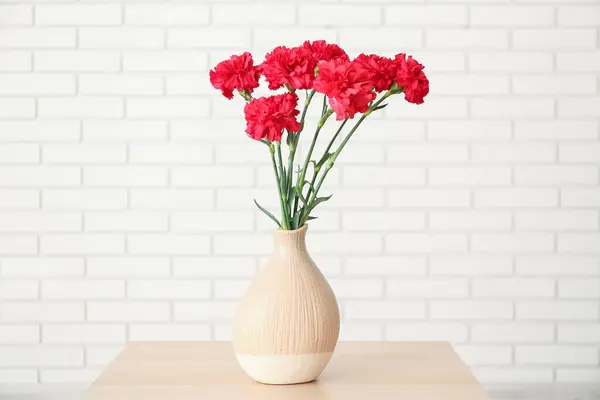 Vaso Com Cravos Vermelhos Mesa Contra Parede Tijolo Branco — Fotografia de Stock