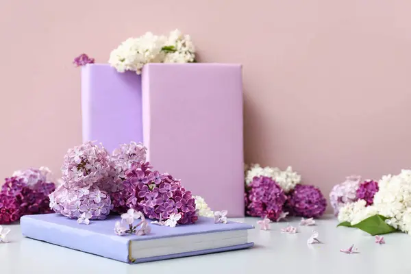 Beautiful fragrant lilac flowers with books on white table near pink wall