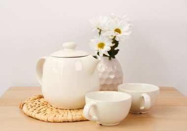 Hasır hasırlı çay seti ve ahşap masada çiçekler.