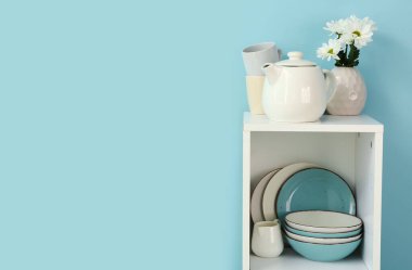 Çaydanlıklı mutfak rafı ve mavi arka planda tabaklar.