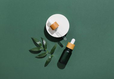 Koyu yeşil arka planda bitki dalı ve pipetli bir şişe kozmetik yağı.