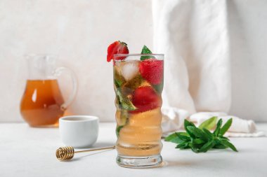 Beyaz arka planda çilekli ve naneli bir bardak buzlu çay.