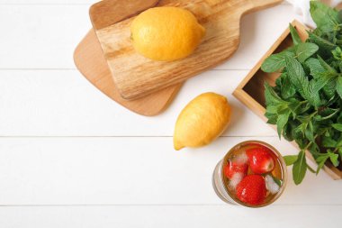 Beyaz arka planda çilekli ve naneli bir bardak buzlu çay.