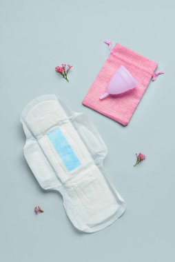 Gri arka planda regl pedi, fincan, çanta ve çiçeklerle kompozisyon