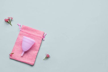 Gri arka planda regl fincanı, çanta ve çiçekli kompozisyon