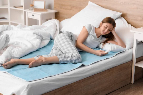 stock image Young woman lying on electric heating pad in bedroom