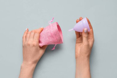 Gri arka planda regl fincanı ve çantası olan bir kadın.