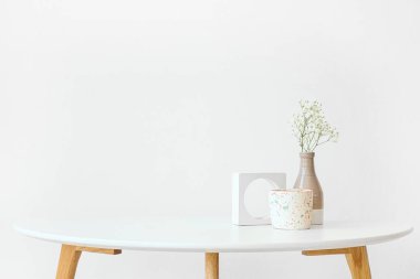 Odadaki ışık duvarının yanındaki masada çikila çiçekleri ve mum.