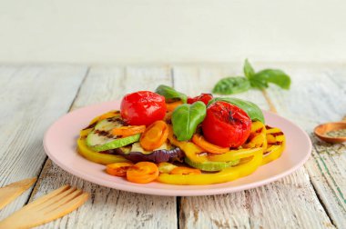 Izgara sebzeli tabak ve beyaz ahşap masada fesleğen.