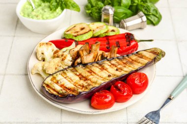 Beyaz fayans masasında ızgara sebze ve fesleğen tabağı.