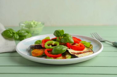 Izgara sebzeli tabak ve yeşil ahşap masada fesleğen.