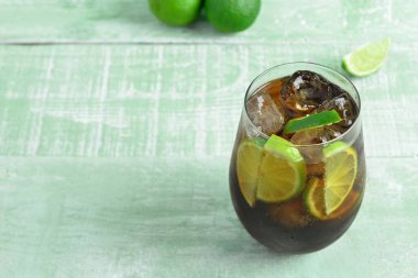Bir bardak soğuk Küba kokteyli ve yeşil ahşap masada limon.