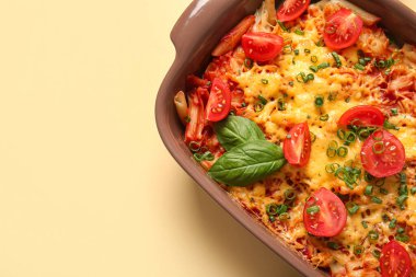 Bej arka planda domates soslu ve peynirli makarna kabı.