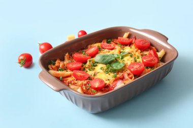 Mavi arka planda domates soslu ve peynirli makarna kabı.