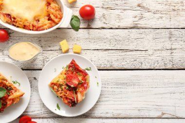 Beyaz ahşap arka planda domates soslu makarna tabakları ve fırın.