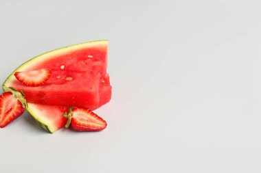 Gri arkaplanda taze karpuz ve çilek parçaları.