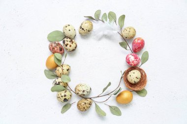 Frame made of Easter quail eggs, feather and eucalyptus branches on white background