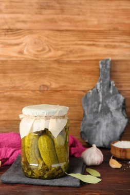 Lezzetli salatalıklı kavanoz ve ahşap masada baharatlar.