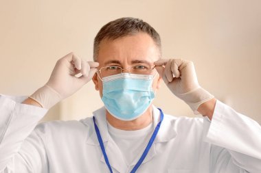 Tıbbi maskeli yetişkin bir erkek doktor ve hastanede gözlüklü, yakın plan.