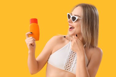 Sarı arka planda güneş kremini gösteren genç bir kadın.