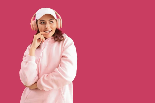 戴着粉色背景耳机的有思想的年轻女人 — 图库照片