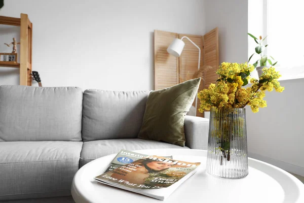 リビングルームでテーブルの上にミモザの花や雑誌と花瓶 — ストック写真