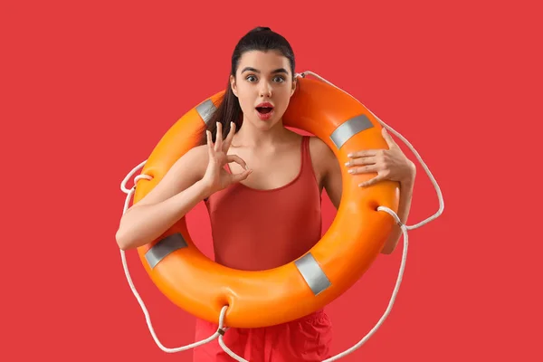 Female lifeguard with ring buoy showing OK on red background