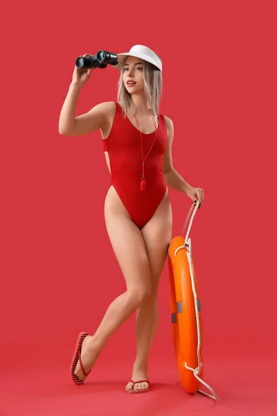 Female lifeguard with binoculars and ring buoy on red background