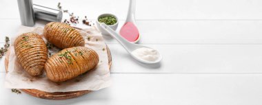 Beyaz ahşap zemin üzerinde lezzetli fırında patates, sos ve baharatlar.