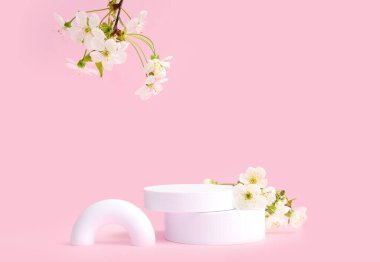 Pembe arka planda dekoratif podyumlar ve çiçek açan dallar