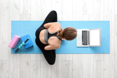 Dizüstü bilgisayarlı genç bir kadın spor salonunda yoga yapıyor.