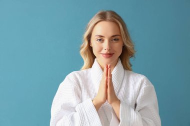 Mavi arka planda yüz geliştirme egzersizi yapan genç bir kadın.