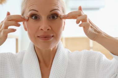 Olgun kadın banyoda yüz geliştirme egzersizi yapıyor, yakın plan.